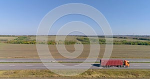 A truck with a red container is driving along the road. A truck with an orange cabin transports a red container view