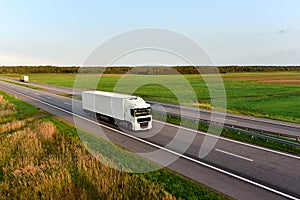 Truck with semi-trailer driving along highway on the blye sky background. Goods delivery by roads. Services and Transport