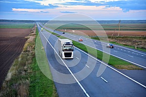 Truck with semi-trailer driving along highway on the sunset background. Goods delivery by roads. Services and Transport logistics