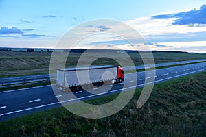 Truck with semi-trailer driving along highway on the sunset background. Goods delivery by roads. Services and Transport logistics