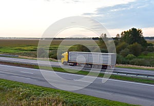 Truck with semi-trailer driving along highway on the sunset background. Goods delivery by roads. Services and Transport logistics