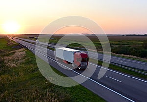 Truck with semi-trailer driving along highway on the sunset background. Goods delivery by roads. Services and Transport logistics