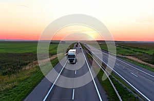 Truck with semi-trailer driving along highway on the sunset background. Goods delivery by roads. Services and Transport logistics