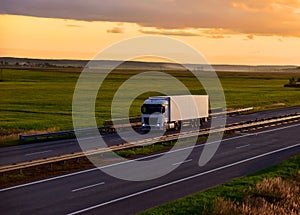 Truck with semi-trailer driving along highway on the sunset background. Goods delivery by roads. Services and Transport logistics