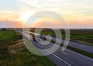 Truck with semi-trailer driving along highway on the sunset background. Goods delivery by roads. Services and Transport logistics