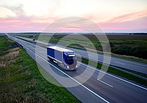 Truck with semi-trailer driving along highway on the sunset background. Goods delivery by roads. Services and Transport logistics