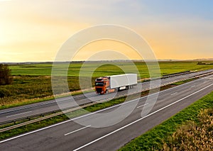 Truck with semi-trailer driving along highway on the sunset background. Goods delivery by roads. Services and Transport logistics