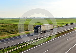 Truck with semi-trailer driving along highway on the sunset background. Goods delivery by roads. Services and Transport logistics