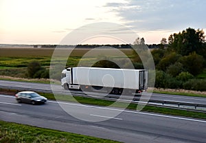 Truck with semi-trailer driving along highway on the sunset background. Goods delivery by roads. Services and Transport logistics