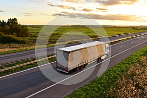 Truck with semi-trailer driving along highway on the sunset background. Goods delivery by roads. Services and Transport logistics