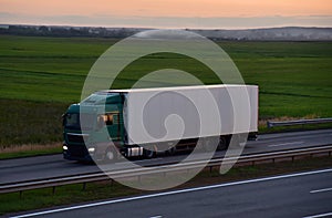 Truck with semi-trailer driving along highway on the sunset background. Goods delivery by roads. Services and Transport logistics