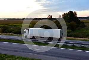 Truck with semi-trailer driving along highway on the sunset background. Goods delivery by roads. Services and Transport logistics