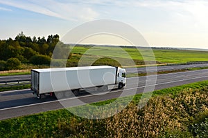 Truck with semi-trailer driving along highway on the sunset background. Goods delivery by roads. Services and Transport logistics