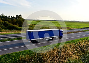 Truck with semi-trailer driving along highway on the sunset background. Goods delivery by roads. Services and Transport logistics