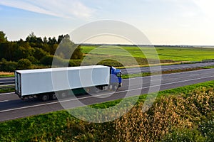 Truck with semi-trailer driving along highway on the sunset background. Goods delivery by roads. Services and Transport logistics