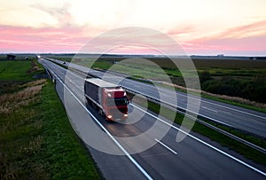 Truck with semi-trailer driving along highway on the sunset background. Goods delivery by roads. Services and Transport logistics