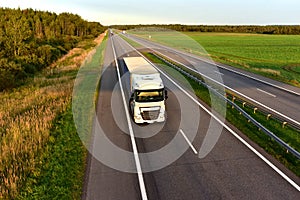 Truck with semi-trailer driving along highway on the sunset background. Goods delivery by roads. Services and Transport logistics