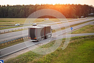 A truck with a semi-trailer and a hitch transports cargo against the backdrop of a sunset along the highway. Bulk cargo