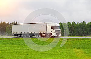 A truck with a semi-trailer transports cargo in summer in cloudy rainy weather on a wet road in the rain. Skidding on