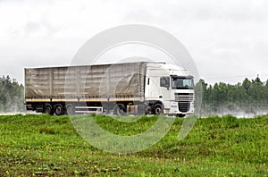 A truck with a semi-trailer transports cargo in the summer on a motorway in rainy weather. Copy space for text