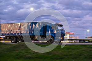 Truck with semitrailer moves along a road past gas station