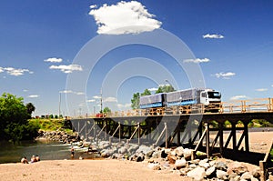 Truck with trailer crossing a bridge over a river.