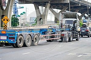 Truck with a trailer and an empty blue long platform rides in the city on the highway under bridge junction