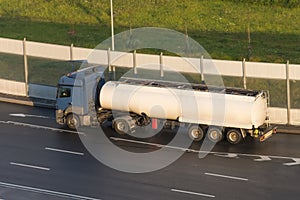 Truck with a trailer white tank on the highway in the sunset light.