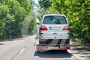 Truck transporter carrying car on road. Back view. Bright green trees along road