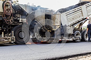 Truck is unloading asphalt to machine for repair road