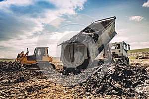 truck unloading garbage at dumping site. Industrial bulldozer, excavator and dumping trucks working photo