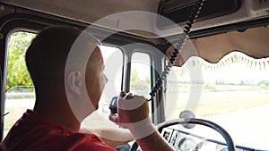 Trucker speaks on radio communication while driving car at sunny day. Lorry driver riding on country road and talking on