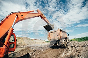 Trucks being loaded during highway construction site. Details of excavator scoop doing earthmoving works. Roadworks