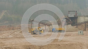 Trucks machine works in the sand ballast quarry on the cloudy summer day