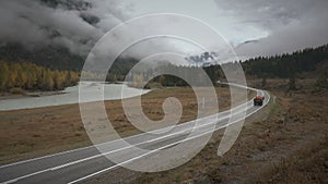 Trucks traveling on a winding road along river on a cloudy autumn rainy day, Siberia, Altai