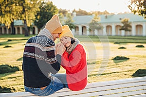 True feelings and romantisism concept. Adorable young woman in knitted yellow hat and red warm sweater warms her hands in boyfrien