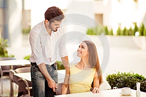 True gentleman! Young handsome brunet lover is adjusting the chair of his happy lady, both well dressed, at a sunny terrace of res
