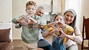 True love. Happy caucasian family, grandparents and grandchildren making heart sign with hands and smiling at camera