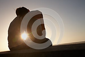 True romance at sunset. Silhouette of a couple sitting beside each other outside.