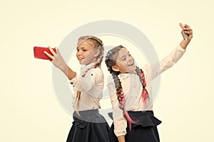 True selfie stars. Happy small schoolgirls taking selfie with smartphones isolated on white. Little children smiling to