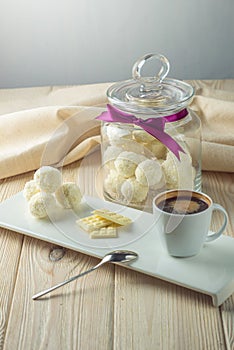 Truffle balls with white chocolate sprinkled with coconut on a saucer next to a jar of candy and a Cup of coffee