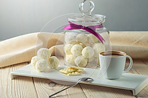 Truffle balls with white chocolate sprinkled with coconut on a saucer next to a jar of candy and a Cup of coffee