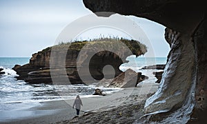 Truman Track, New Zealand,  October 8, 2019: Beautiful image of blonde European girl walking on a beach with a rock formation in