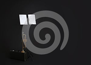 Trumpet, case and note stand with music sheets on black. Space for text