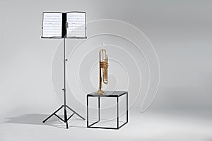 Trumpet and note stand with music sheets on grey. Space for text