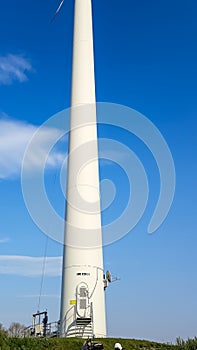 The trunk of a very tall white wind turbine photographed against a bright blue sky from an interesting worm\'s eye view. Frog