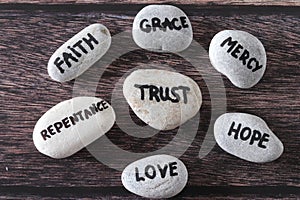 Trust, mercy, faith, grace, love, repentance, and hope handwritten words on stones, top view.