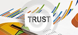 TRUST text on paper on chart background with pen