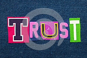 TRUST text word collage in brightly colored fabric on blue denim, confidence and fidelity