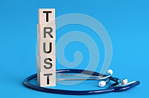 TRUST word written on wooden blocks and stethoscope on light blue background